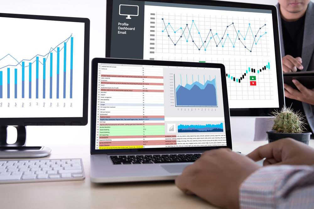 Professional sitting at desk staring at 3 computers screens with charts on them.