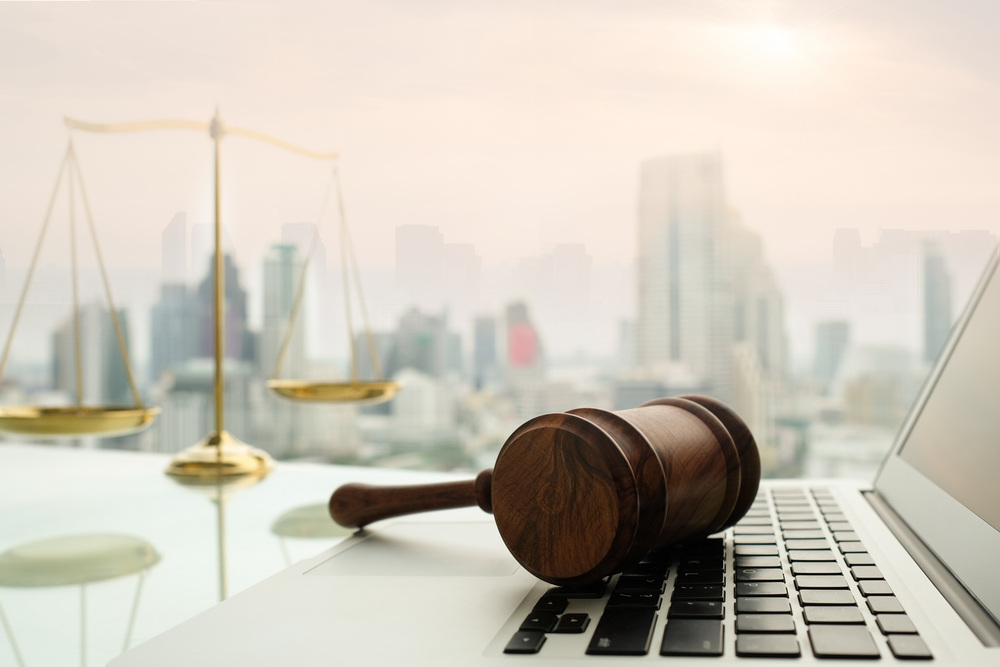 Gavel on a laptop with justice scale and cityscape in background.