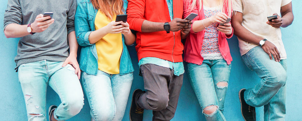 Group of young people leaning against a wall on their mobile devices.