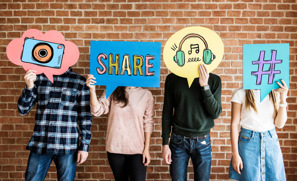 Four people standing holding signs with images like a camera, a hashtag, etc.