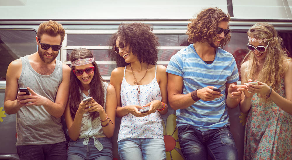 A group of young people at the subway looking at their phones and having a good time.